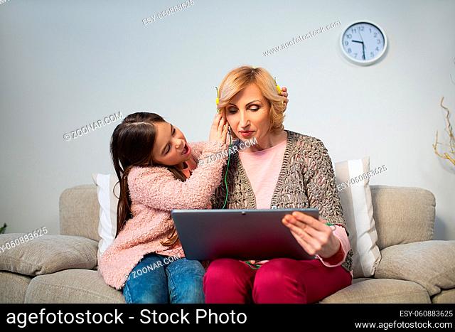 Little girl fixing headphones for granny. Sitting together on sofa