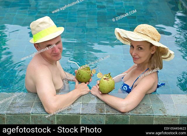Happy couple in the pool drinks coconut milk through a straw