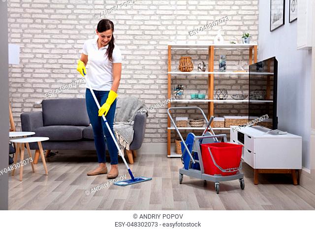 Female Janitor Cleaning Floor With Mop In Living Room