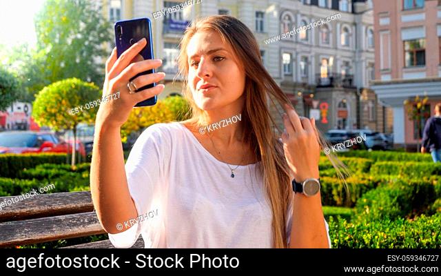 Portrait of beautiful young woman making selfie photo on smartphone in park