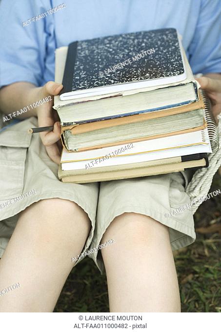 Child holding stack of books and notebooks on lap