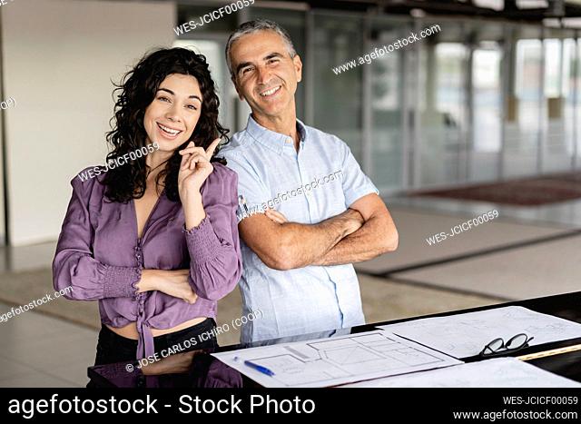 Smiling businesswoman pointing at colleague standing with arms crossed at office