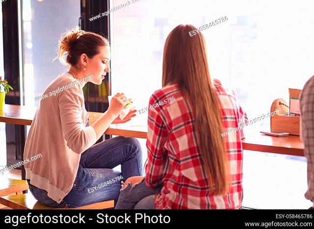 Toned picture of pretty women eating sandwiches and drinking coffee during break. Ladies spending time in cafe or restaurant