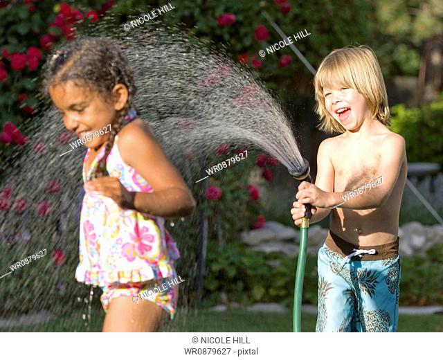 little boy spraying a little girl with the hose
