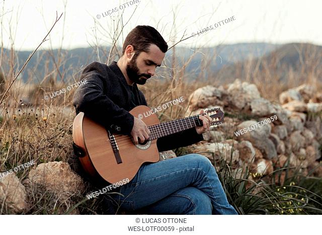 Male musician with beard playing the guitar in the countryside