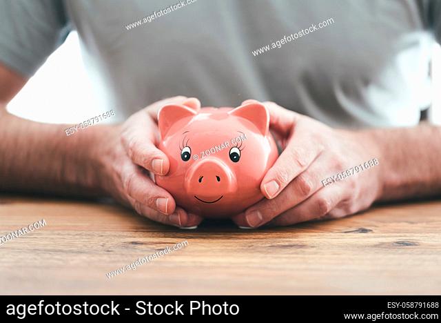 close-up view of man holding piggy bank with both hands at wooden table, saving money and finance concept