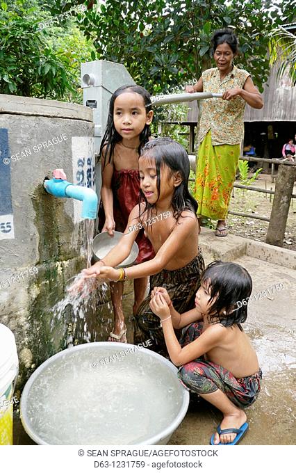 CAMBODIA. Sorn Thong Pin 55 using hand pump to get water from her well, while her grandaughters Chenda 6, San Samey 7 and Chanthou 9 take a bath, Sesan village
