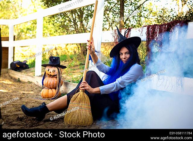 A girl dressed as a witch sits by the fence, thick white smoke creeps out from behind the fence