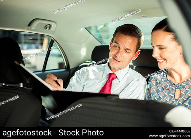 Businessman and businesswoman working in back seat of car