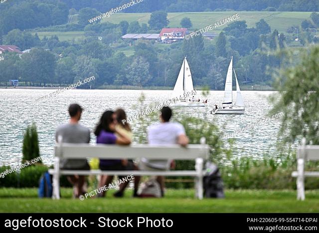 05 June 2022, Baden-Wuerttemberg, Ìberlingen Am Bodensee: Two boats sail just before a rain shower off Ìberlingen, while in the foreground people sit on a park...