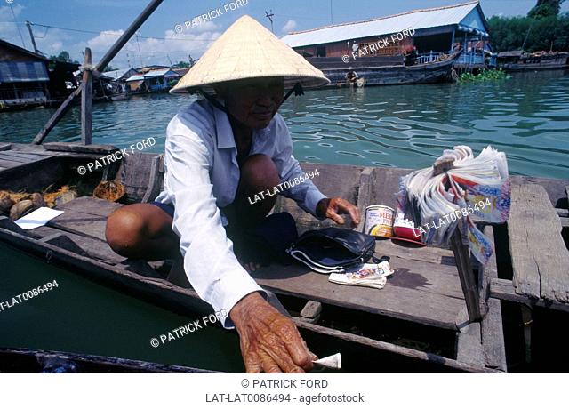 Mekong delta. Man in shallow boat. Lottery tickets for sale. Bundles of currency, banknotes. Houseboat. DwellingsGames, board games