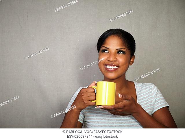 Young african woman in her 20s holding a tea cup while standing against grey background