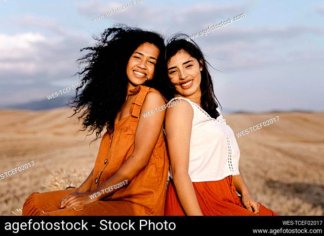 Smiling female friends sitting back to back in farm