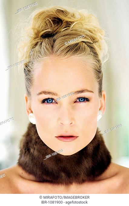 Blue-eyed blonde young woman in her twenties with an elegant hairstyle staring intensively into the camera