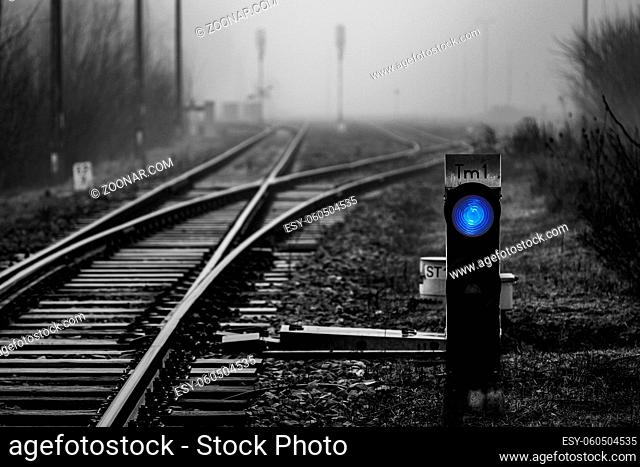 Railway signal with blue light with railroad junction disappearing in mist, monochrome image with blue colour