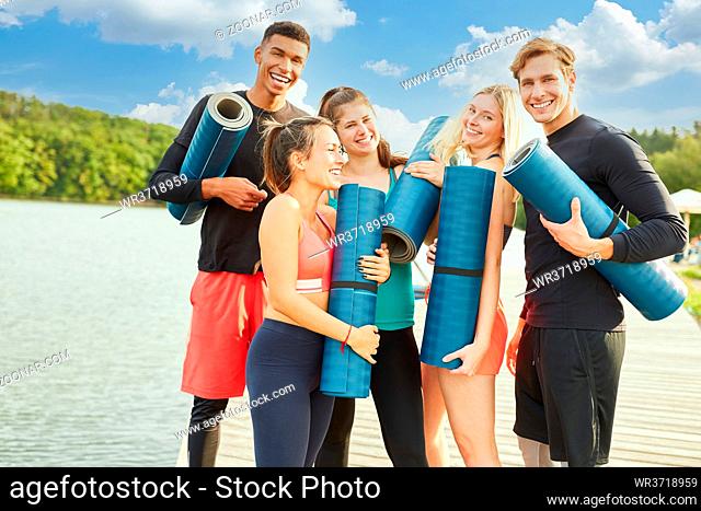 Glückliche Gruppe Freunde beim Yogakurs am See im Sommer mit Yogamatte