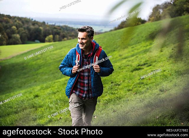 Happy mature man walking with backpack on meadow