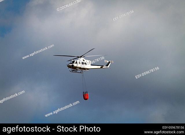 Fire fighting helicopter with bambi basket loaded with water on it's way to a fire
