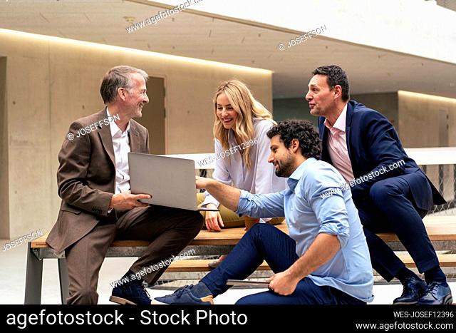 Happy business colleagues discussing over laptop in office