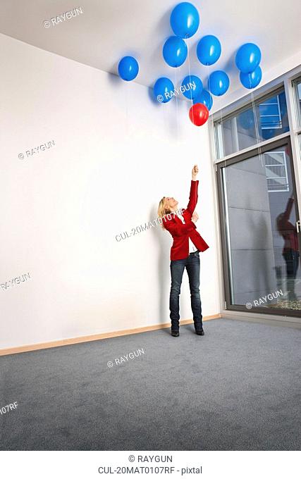 Woman picking red balloon from ceiling