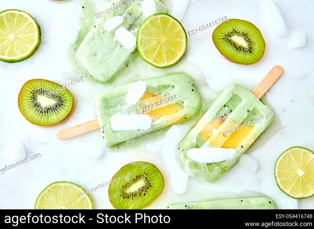 Frozen fruit smoothies with a slice of mango presented on a gray background with pieces of ice, kiwi and lime. Healthy summer dessert. Flat lay