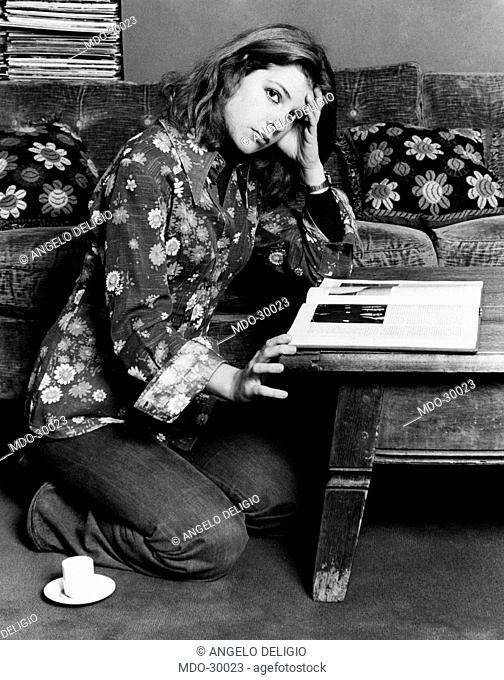 Pamela Villoresi down on her knees. The Italian actress Pamela Villoresi sitting on the ground on her knees reading a book. Milan, 1970s