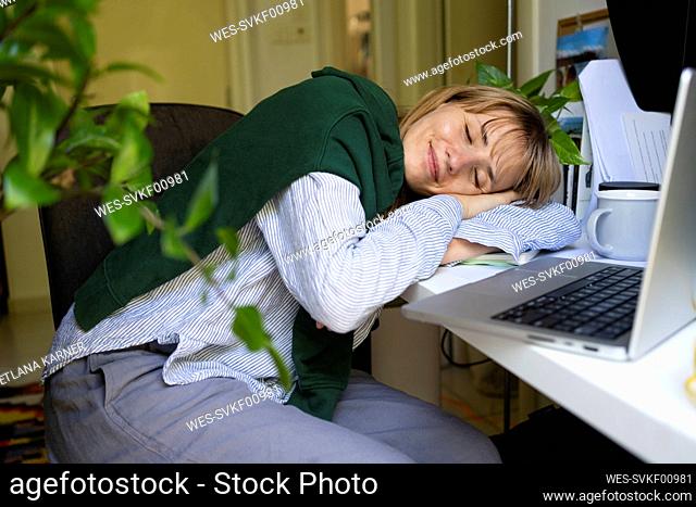Smiling freelancer sleeping on table at home