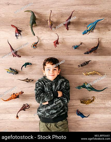 Portrait of smiling little boy lying on the floor between toy dinosaurs