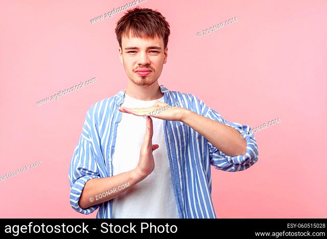 I need more time. Portrait of upset brown-haired man with small beard and mustache in casual striped shirt showing time out gesture, asking pause