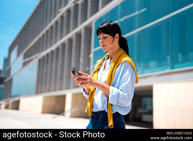 Mature businesswoman using smart phone in front of building