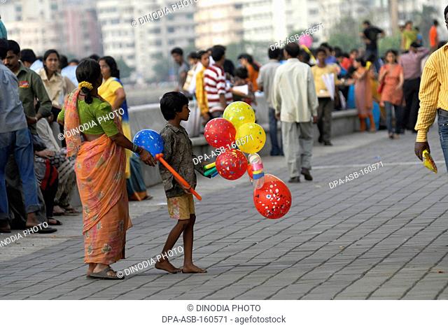 Young boy along with his mother sells colourful balloons to tourists visiting Marine Drive in Bombay Mumbai ; Maharashtra ; India