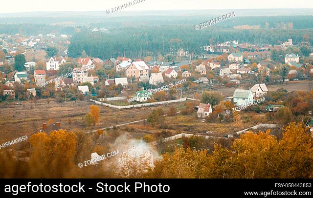 Panoramic view from the mountain to the cottage town, green lawns and coniferous forests on the horizon. Trees with colorful fall foliage in foreground