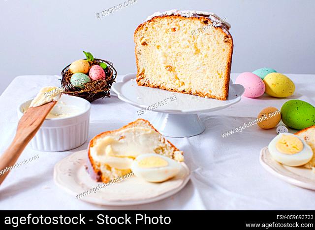 Close-up holiday served table, preparation for traditional Easter brunch. Easter cake cut into pieces, colored eggs, bowl with butter