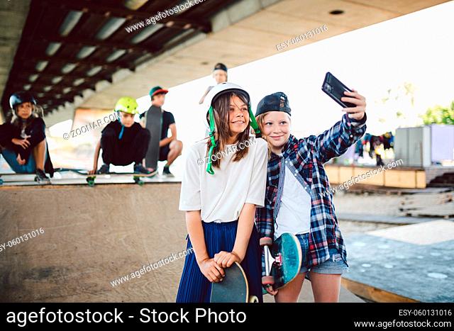 Hipster girlfriends taking selfie on ramp in the skate park. Two girls skateboarder friends taking photo portrait with mobile phone in the street skatepark