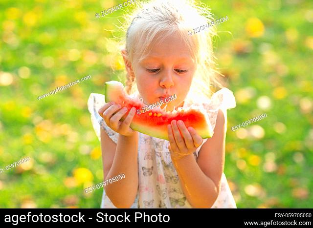Cute blond little girl with watermelon on the grass in park