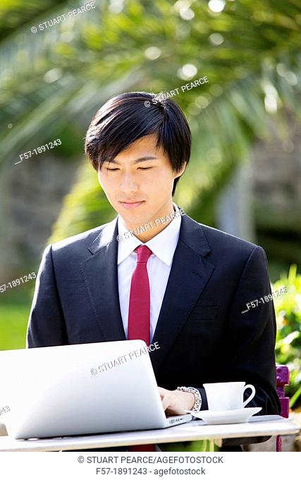 Young Asian man working on his laptop computer outside