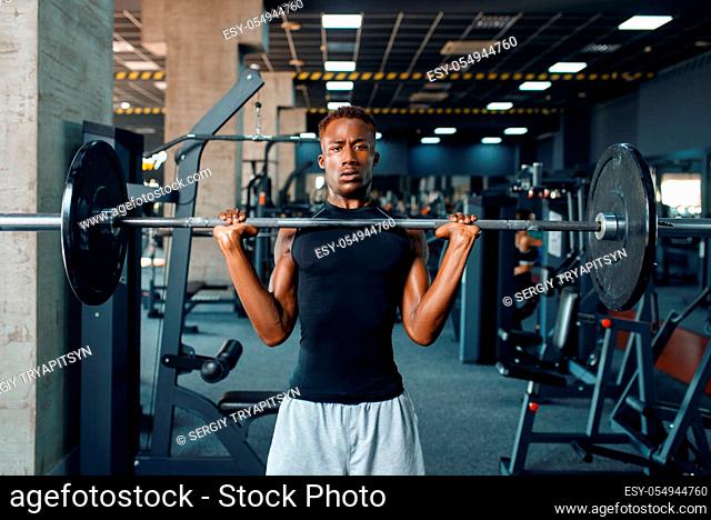 Muscular athlete in sportswear doing exercise with barbell on training in gym. Workout in sport club, healthy lifestyle