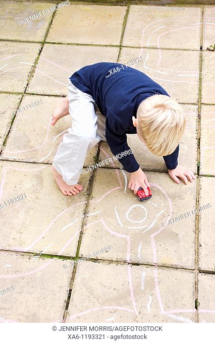 A young boy plays with his toy car on roads drawn on patio slabs with chalk
