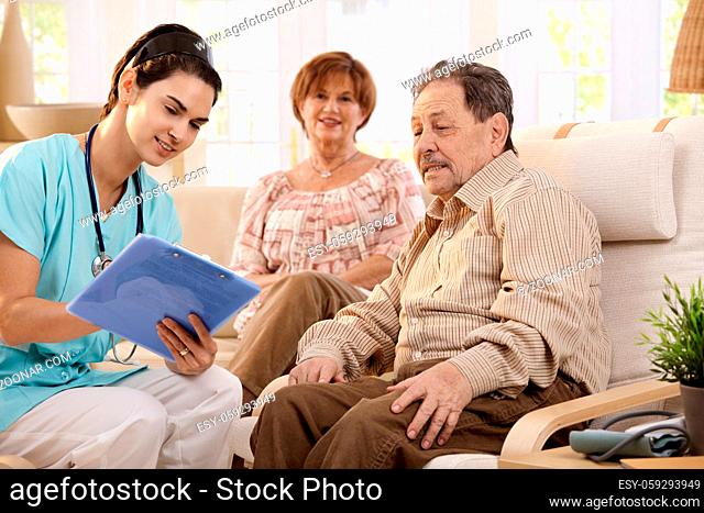 Nurse talking with elderly people and making notes during examination at home, smiling