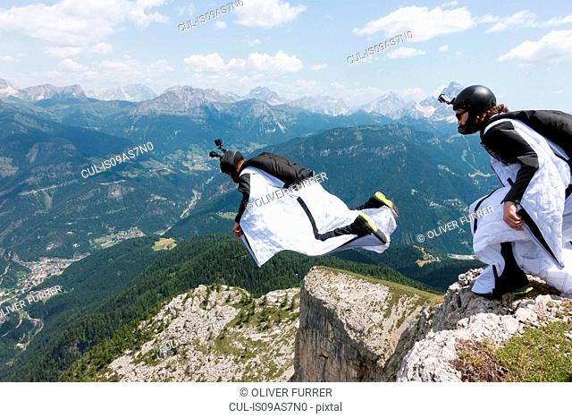 Two male BASE jumpers exiting from mountain top, Dolomites, Italy