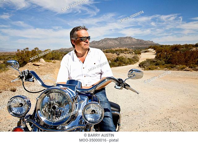 Senior man wearing sunglasses on motorcycle in desert