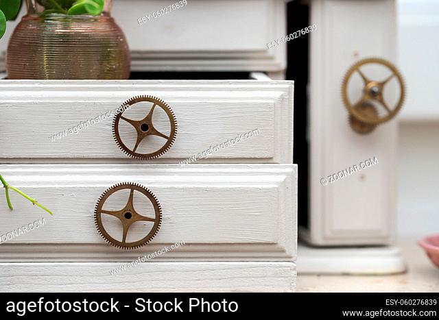 Detail of white miniature cupboard with toothed wheels as drawer knobs