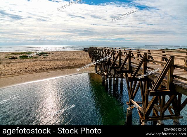 A long wooden boardwalk pier leads from one beach to another over a small ocean inlet