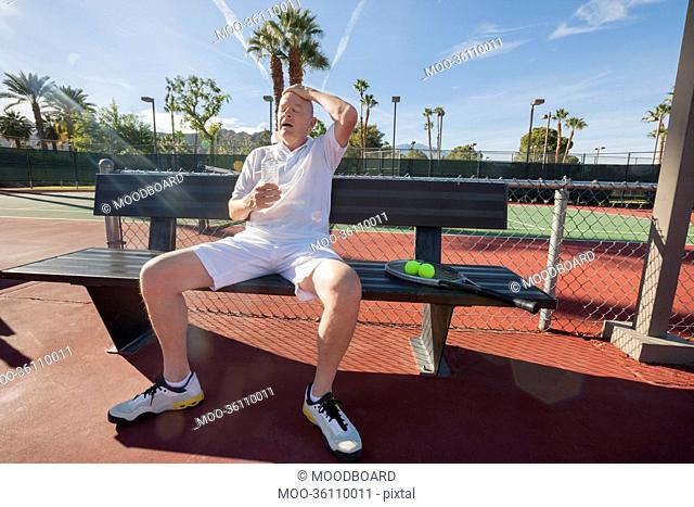 Tired senior tennis player relaxing on bench at court