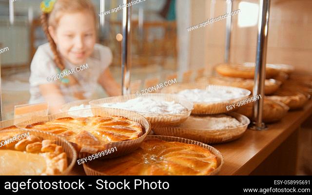 Girl with a pigtail looks at the pies in the window choosing, the girl on the other hand showcases, de-focused view