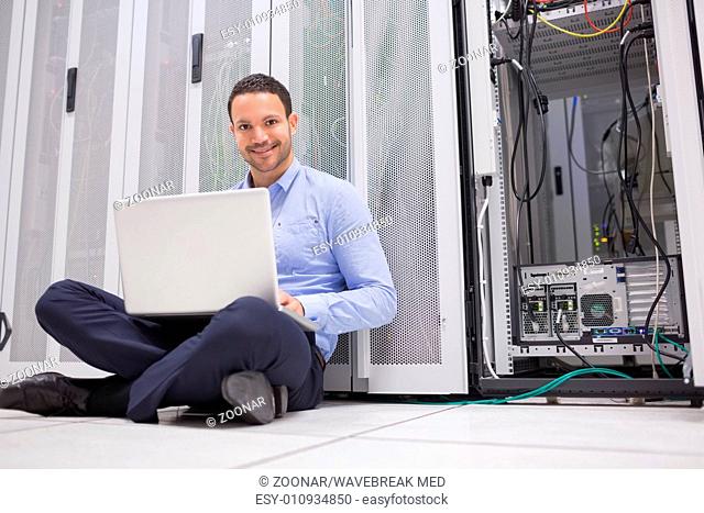 Smiling man sitting on floor checking servers with laptop