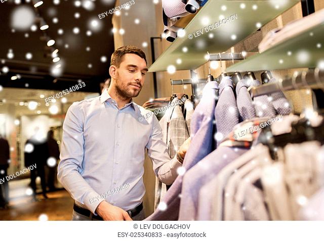 sale, shopping, fashion, style and people concept - happy young man in shirt choosing jacket in mall or clothing store over snow