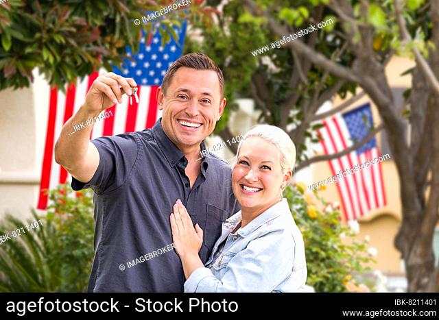Happy couple with new house keys in front of houses with american flags