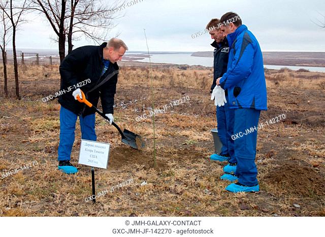 Behind the Cosmonaut Hotel crew quarters in Baikonur, Kazakhstan, Expedition 46-47 crewmember Tim Kopra of NASA (left) plants a tree at a site bearing his name...