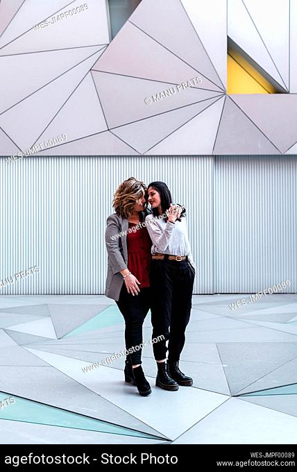 Romantic lesbian couple standing on footpath against modern building in city